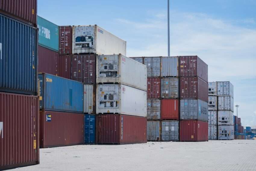 Stacks of shipping containers at a port under a blue sky